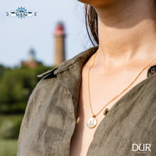 Laden Sie das Bild in den Galerie-Viewer, Frau trägt vergoldete Kette mit vergoldetem Anhänger „Kap Arkona“ aus 925er Silber und echtem Strandsand von DUR Schmuck, im Hintergrund die Leuchttürme von Kap Arkona auf Rügen.